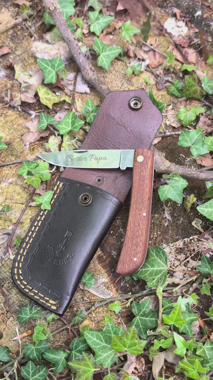 Hippekniep Taschenmesser mit Holzgriff und individueller Gravur liegt auf moosigem Holz in natürlicher Outdoor-Umgebung.